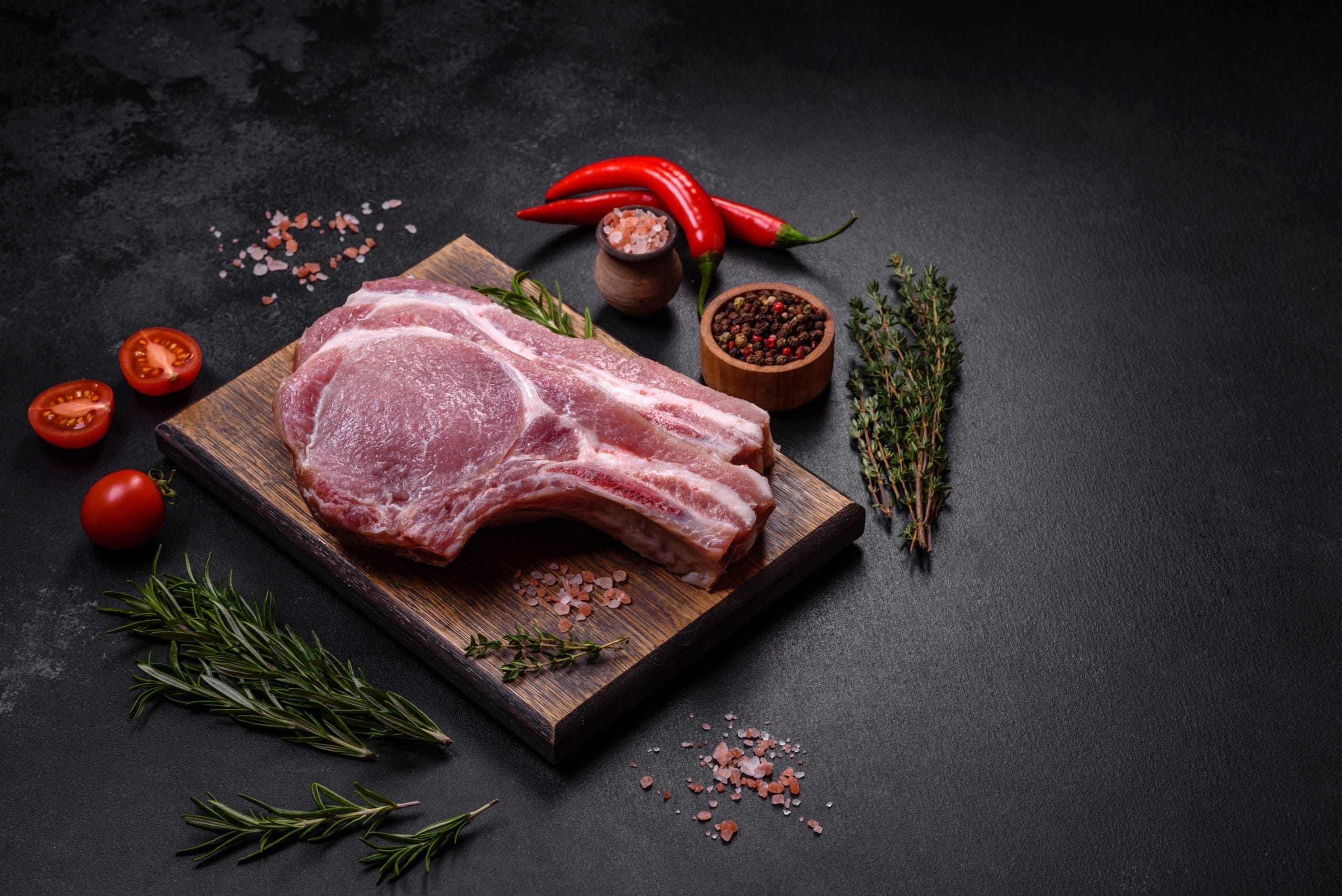 Fresh raw pork meat on the ribs with spices and herbs on a wooden cutting board on a dark concrete background
